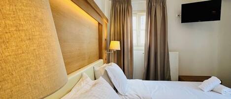 Ein Hotelzimmer mit zwei Betten, einem an der Wand montierten Fernseher und einem Fenster mit Vorhängen.