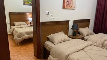 A hotel room with two beds, wooden headboards, a nightstand with a lamp, and a painting on the wall.