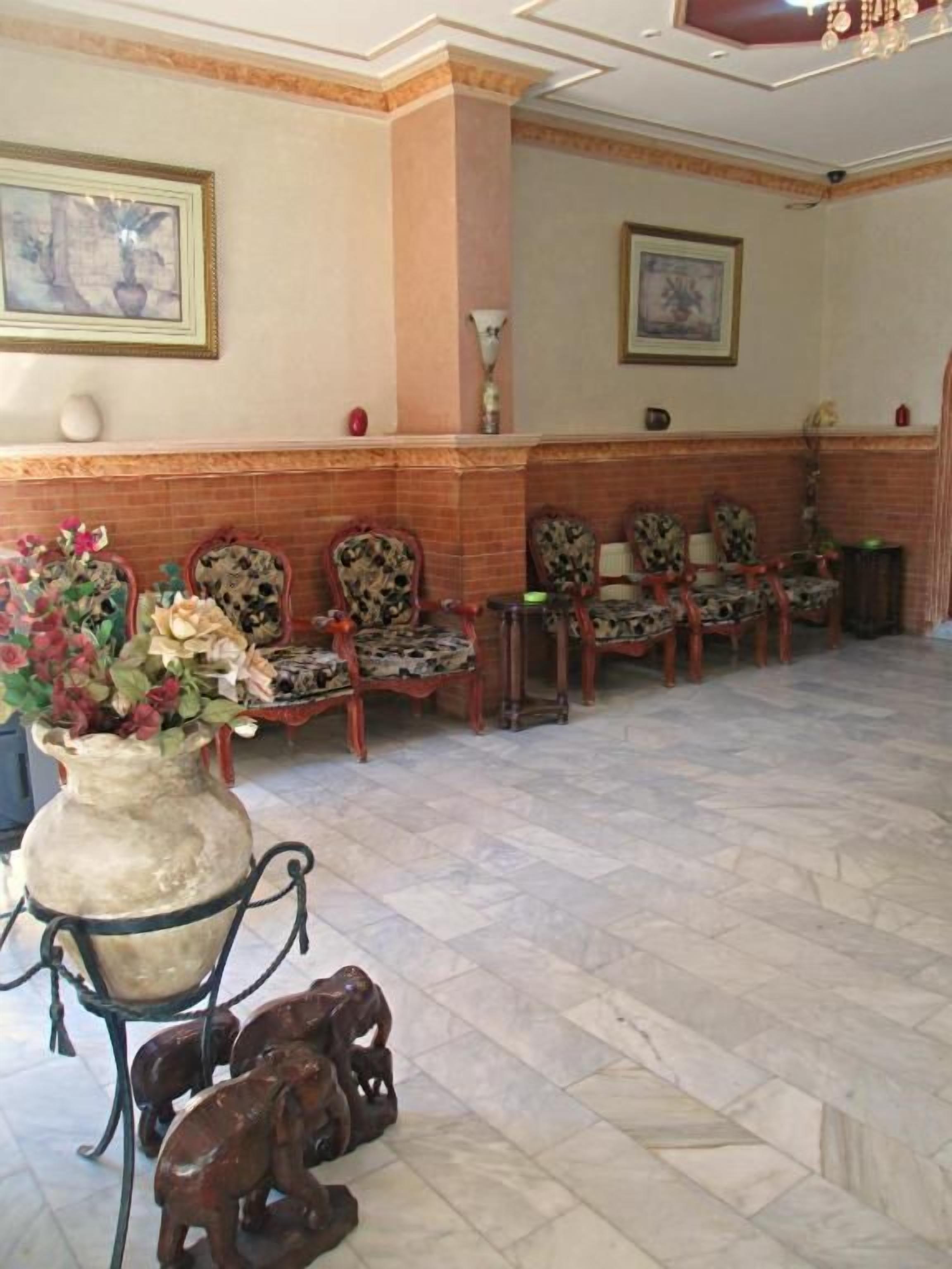 Un hall d’entrée avec un comptoir de réception, plusieurs chaises, un grand vase rempli de fleurs et un sol carrelé.