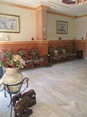 A lobby with a reception desk, several chairs, a large vase with flowers, and a tiled floor. - Sufara Hotel Suites (Amman)