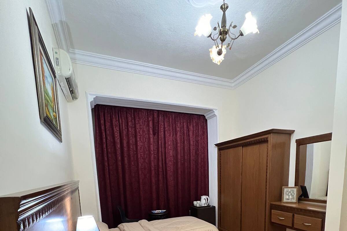 Een slaapkamer met een bed, nachtkastje, lamp, kledingkast en plafondventilator.