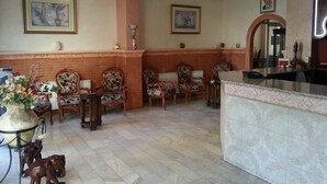 A lobby with a reception desk, several chairs, a chandelier, and framed artwork on the walls.