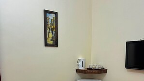 A small room with two black chairs, a small table, a white refrigerator, a mounted television, and a framed picture on the wall.