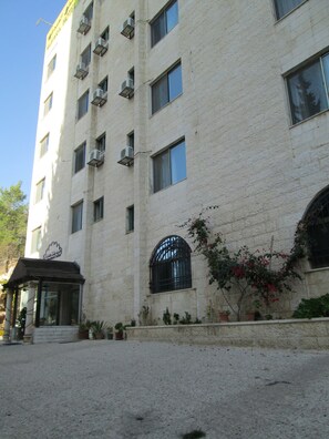 A multi-story building with a central entrance, air conditioning units, and potted plants. - Sufara Hotel Suites (Amman)