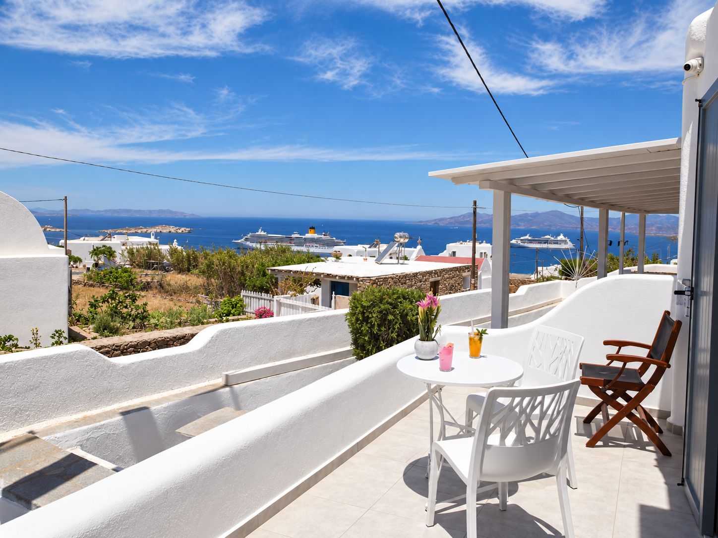 A balcony with a table and chairs, overlooking a coastal view with buildings and a cruise ship.