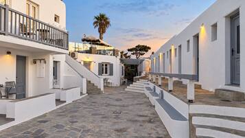 Un patio estrecho empedrado con edificios blancos, una escalera y asientos al aire libre.