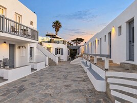 Un patio estrecho empedrado con edificios blancos, una escalera y asientos al aire libre.
