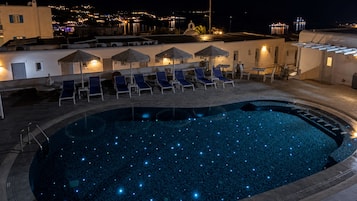 Una piscina nocturna con luces similares a estrellas, sillas de descanso y sombrillas.