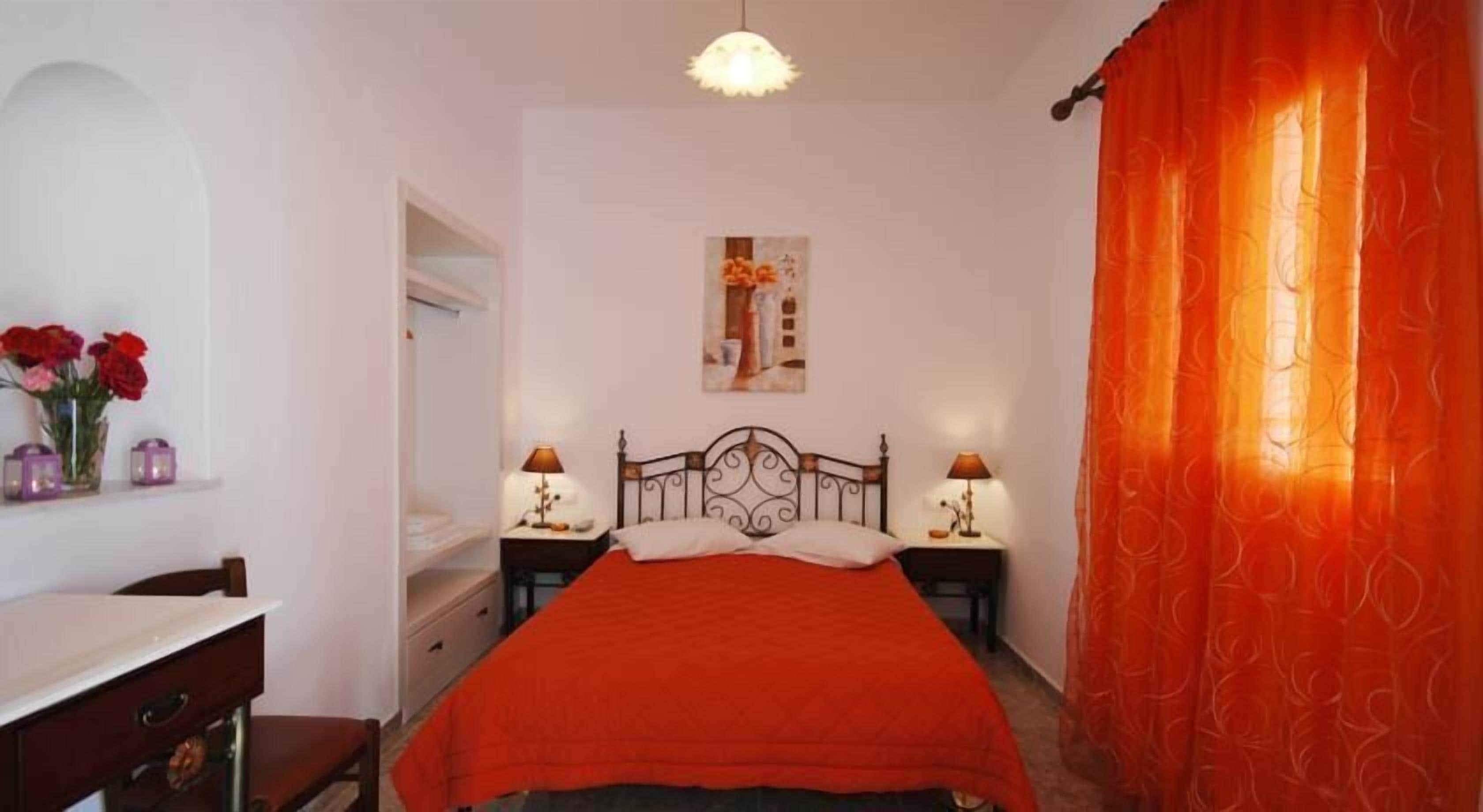 Quarto com cama, duas mesas de cabeceira com abajures, cômoda, espelho e janela com cortinas laranja.