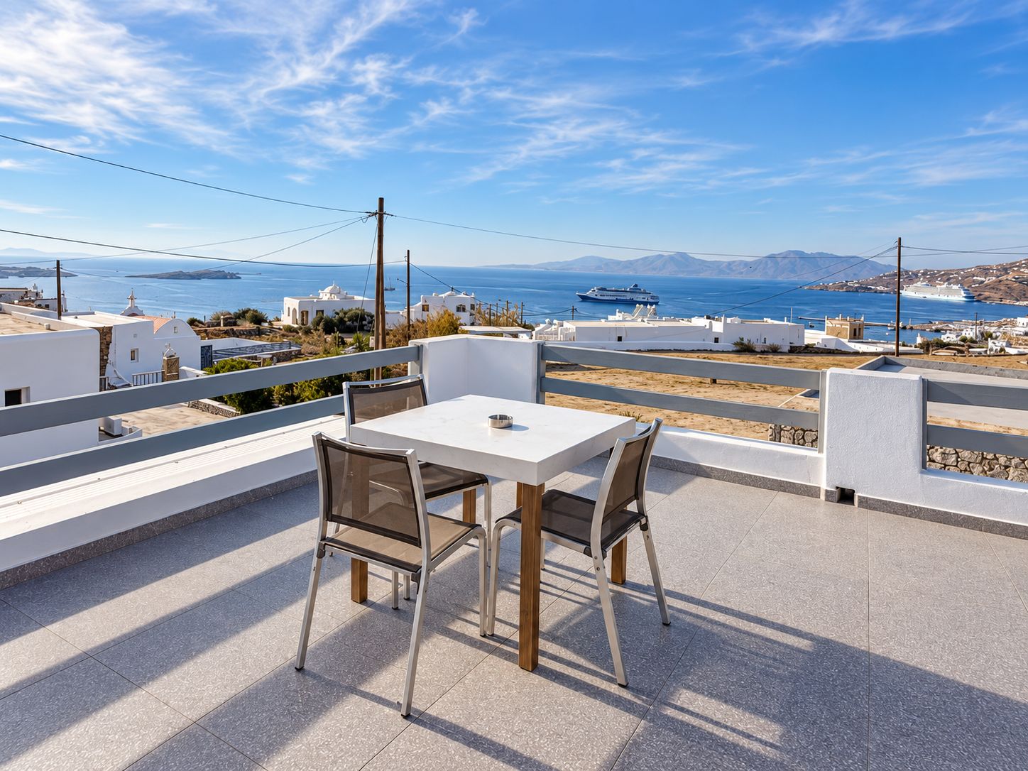 A terrace with a table and chairs overlooking a coastal view with buildings and boats.