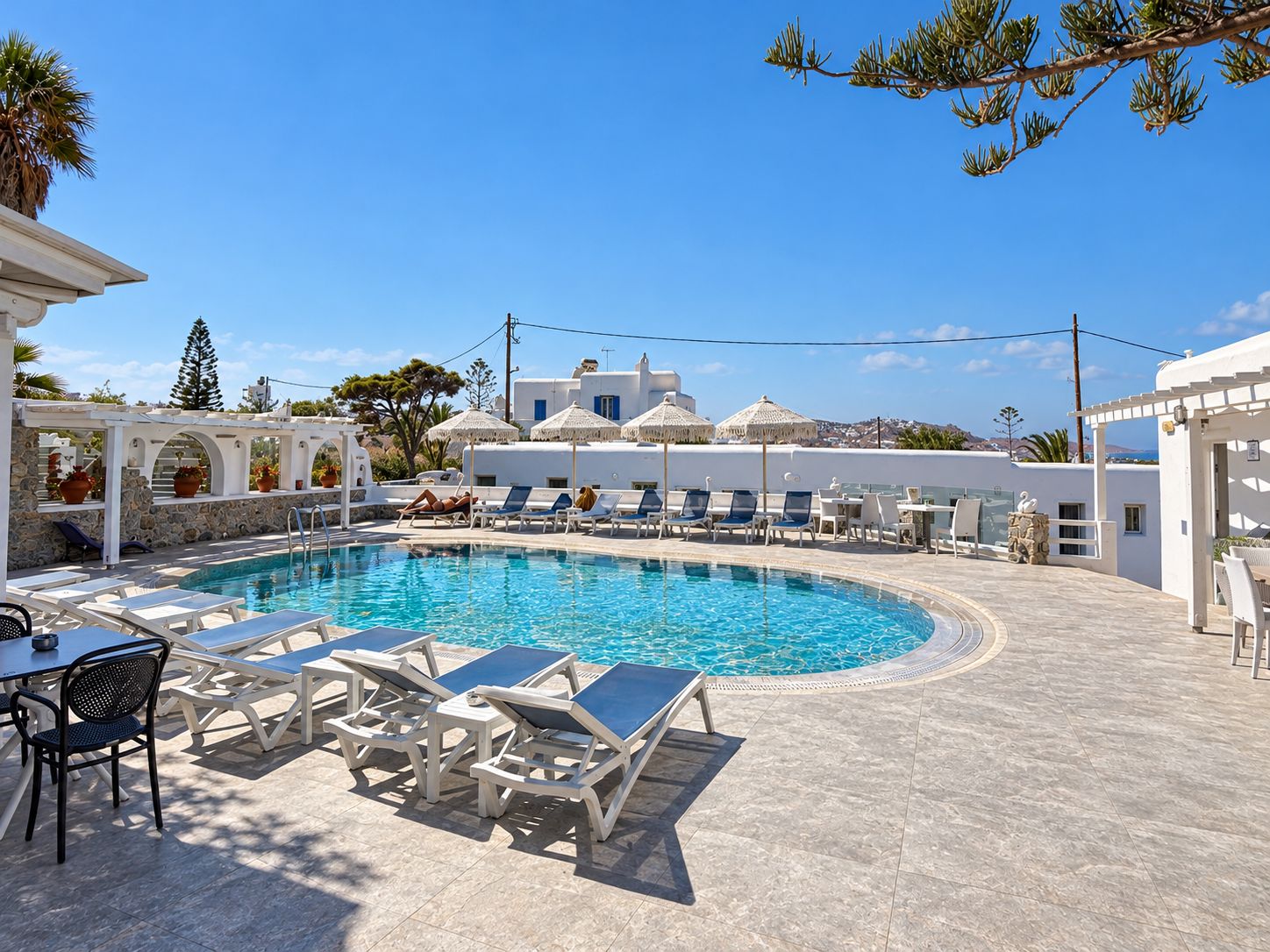 A pool area with lounge chairs and a table, surrounded by white buildings with blue accents.