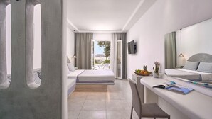 A modern hotel room with a balcony, a desk with a chair, and a bed with a TV on the wall. - Sofia Village (Mykonos)