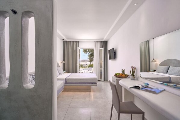 A modern hotel room with a balcony, a desk with a chair, and a bed with a TV on the wall. - Sofia Village (Mykonos)
