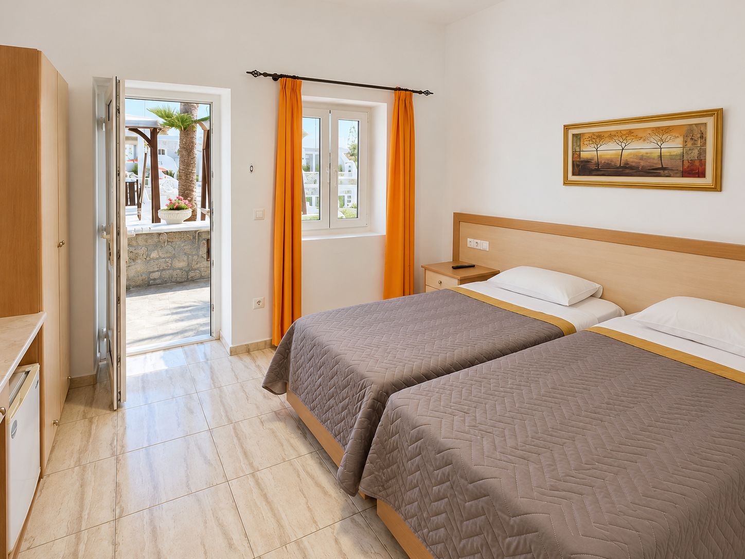 Habitación de hotel con dos camas, un cuadro en la pared y vistas a través de una puerta abierta.