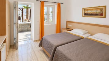 Habitación de hotel con dos camas, un cuadro en la pared y vistas a través de una puerta abierta.