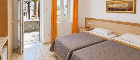 A hotel room with two beds, a painting on the wall, and a view through an open door.