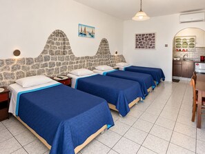 Habitación de hotel con cuatro camas, una pared decorativa de piedra, un cuadro, una zona de cocina y suelo de baldosas.