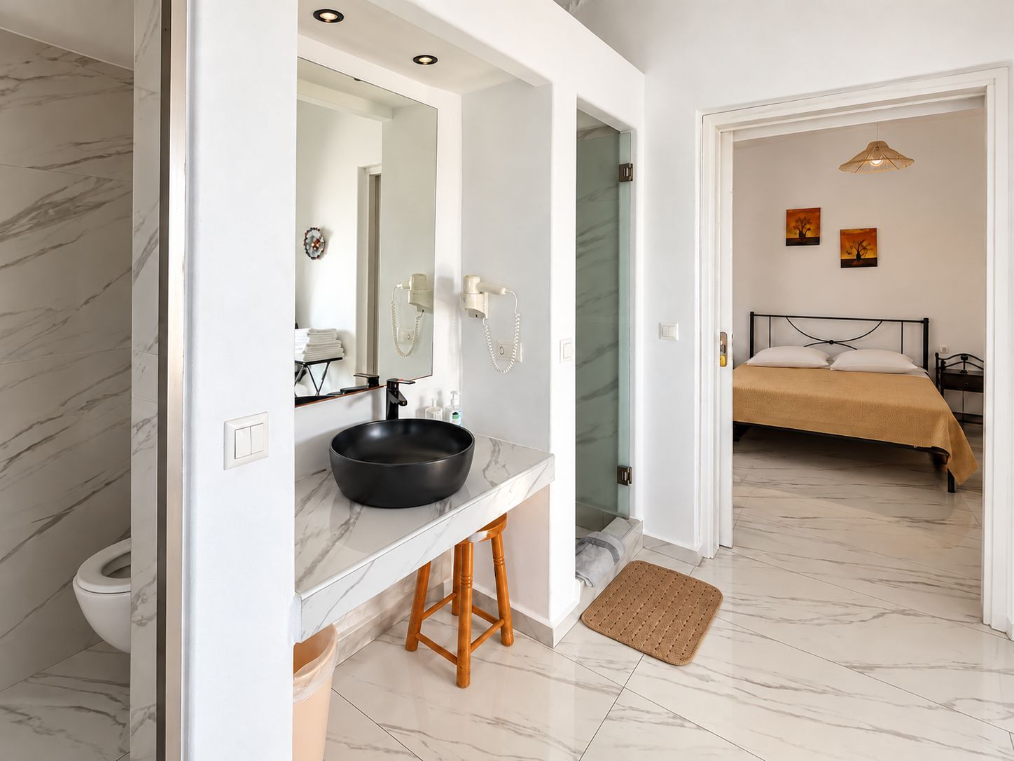 Un baño moderno con piso de mármol, un lavamanos negro y un taburete de madera.