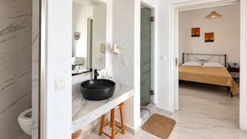 Un baño moderno con piso de mármol, un lavamanos negro y un taburete de madera.