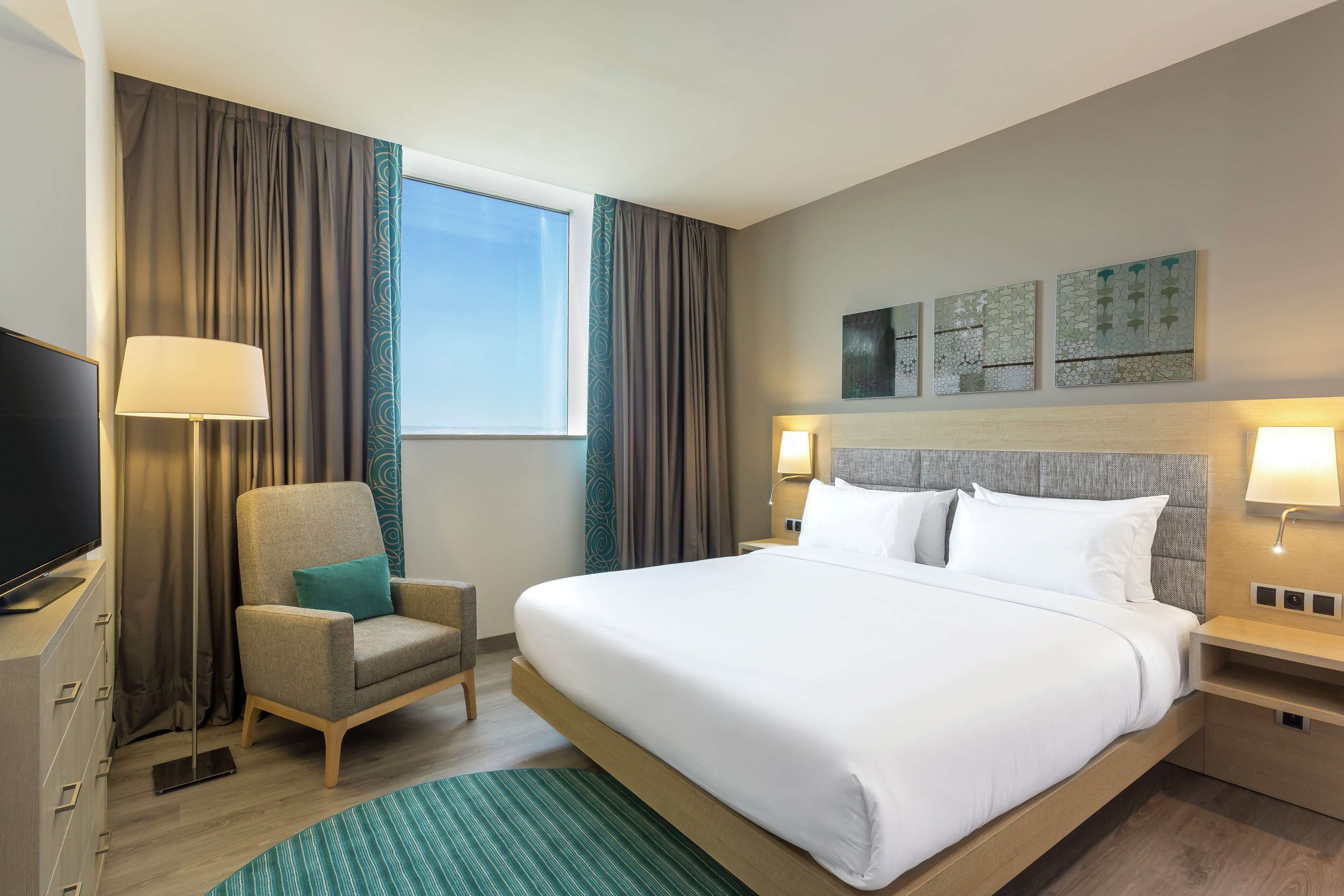 Une chambre d’hôtel moderne avec un grand lit, une chaise, une télévision et des œuvres d’art accrochées au mur.