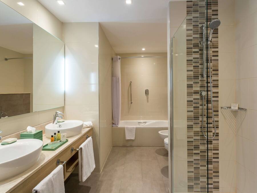 Un baño moderno con dos lavamanos, cabina de ducha con paredes de vidrio y bañera independiente.