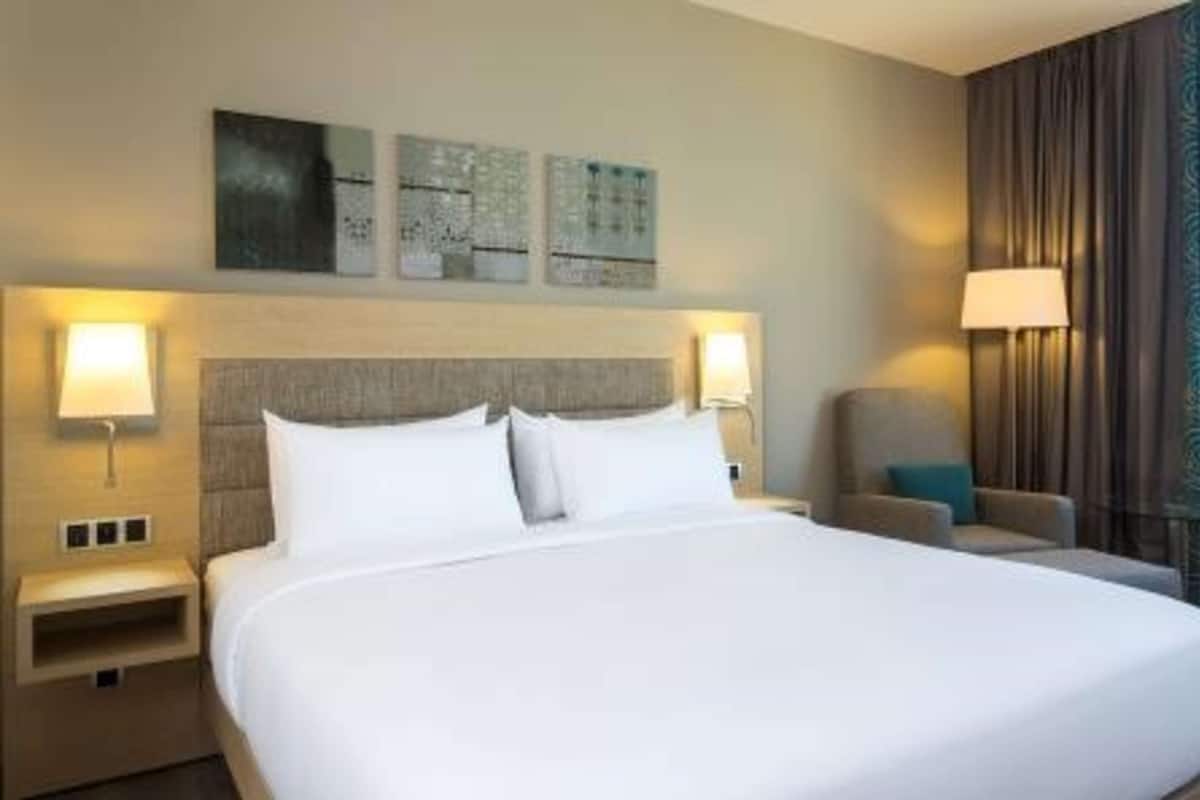 A hotel room with a large bed, two bedside lamps, a chair, and artwork on the wall.