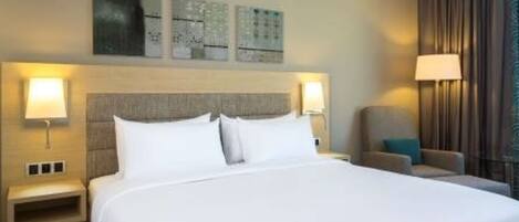 A hotel room with a large bed, two bedside lamps, a chair, and artwork on the wall.