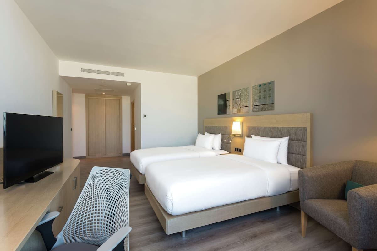 A hotel room with two beds, a TV, a desk, and a chair.
