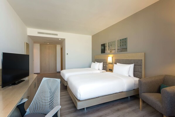 A hotel room with two beds, a TV, a desk, and a chair.