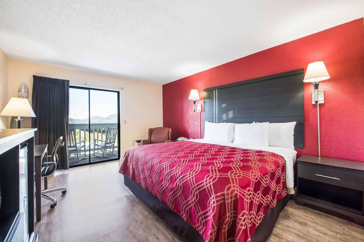 A hotel room with a large bed, a desk, a chair, and a view of the outdoors.