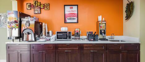 Uma estação de café com máquina de café, micro-ondas e dispensador de suco.
