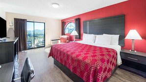 A hotel room with a large bed, a desk, a chair, a TV, a window with curtains, and a view of the outdoors. - Econo Lodge Waynesville (Waynesville)