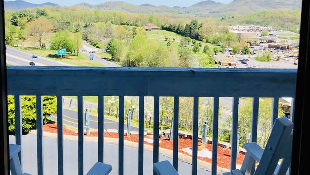 A balcony with white chairs, a view of a green landscape with trees and a building, and a clear blue sky. - Econo Lodge Waynesville (Waynesville)