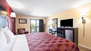 A hotel room with a large bed, a desk with a chair, a television, and a refrigerator.