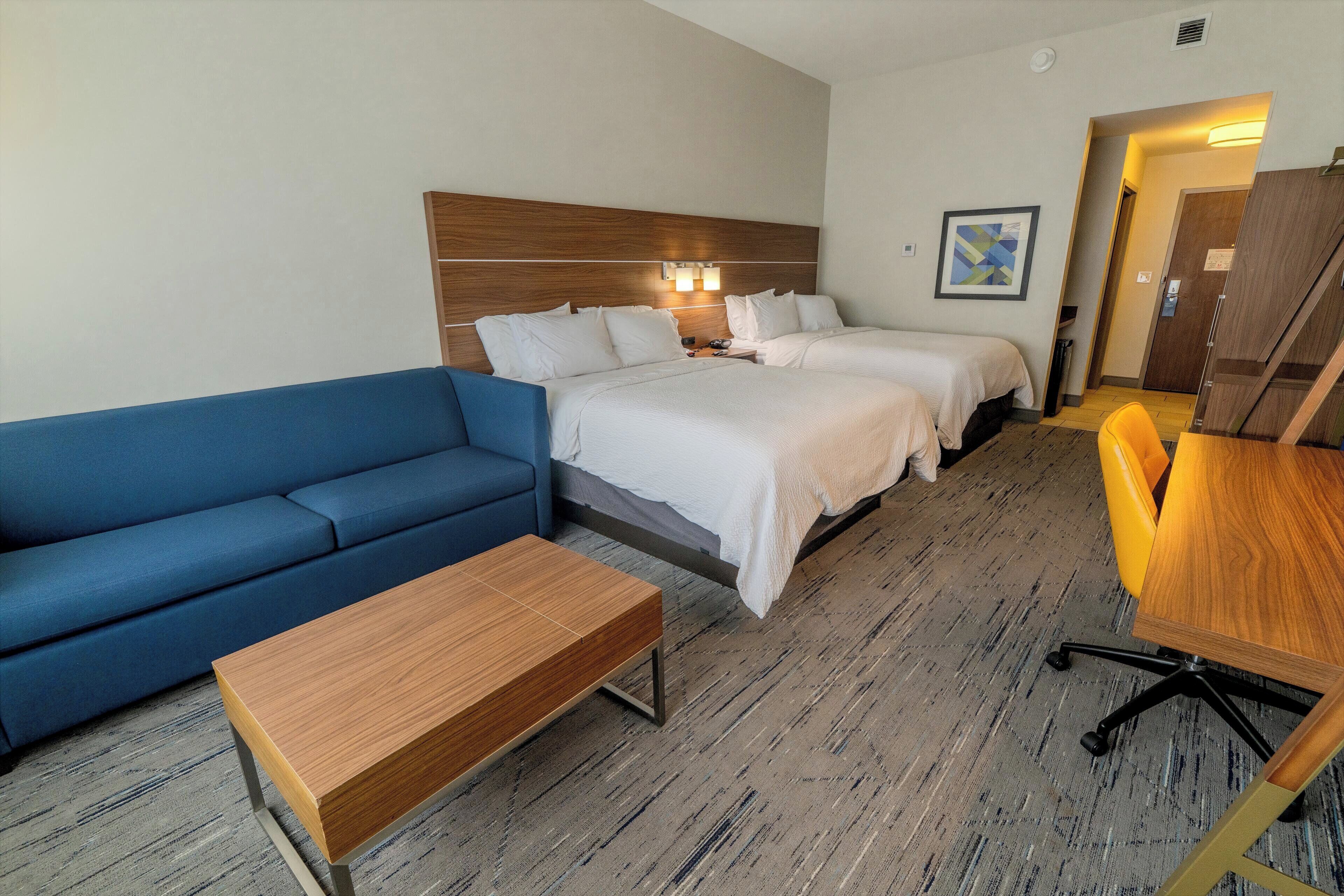 Hotellihuoneessa on sininen sohva, kaksi erillistä sänkyä, puinen pöytä ja työpöytä tuolilla.