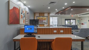 A reception desk with a computer, two orange chairs, and a wall with artwork. - Holiday Inn Express Jasper by IHG (Jasper)