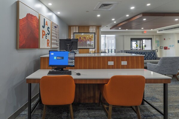 Eine Rezeption mit einem Computer, zwei orangefarbenen Stühlen und einer Wand mit Kunstwerken.