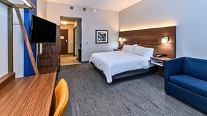 A hotel room with a bed, a desk, a chair, a TV, a blue sofa, and a wooden headboard. - Holiday Inn Express Jasper by IHG (Jasper)