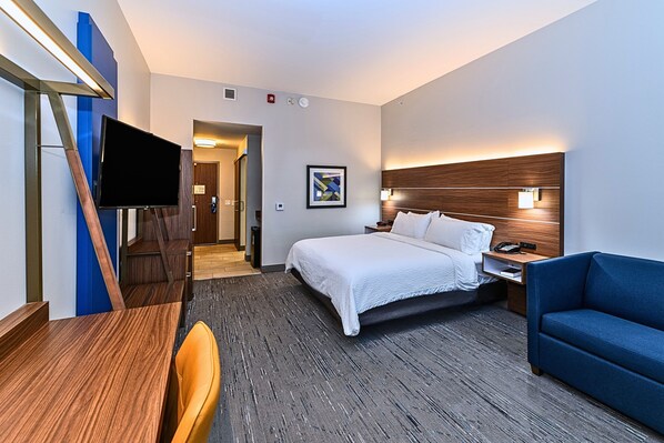 Habitación de hotel con cama, escritorio, silla, televisor, sofá azul y cabecera de madera.