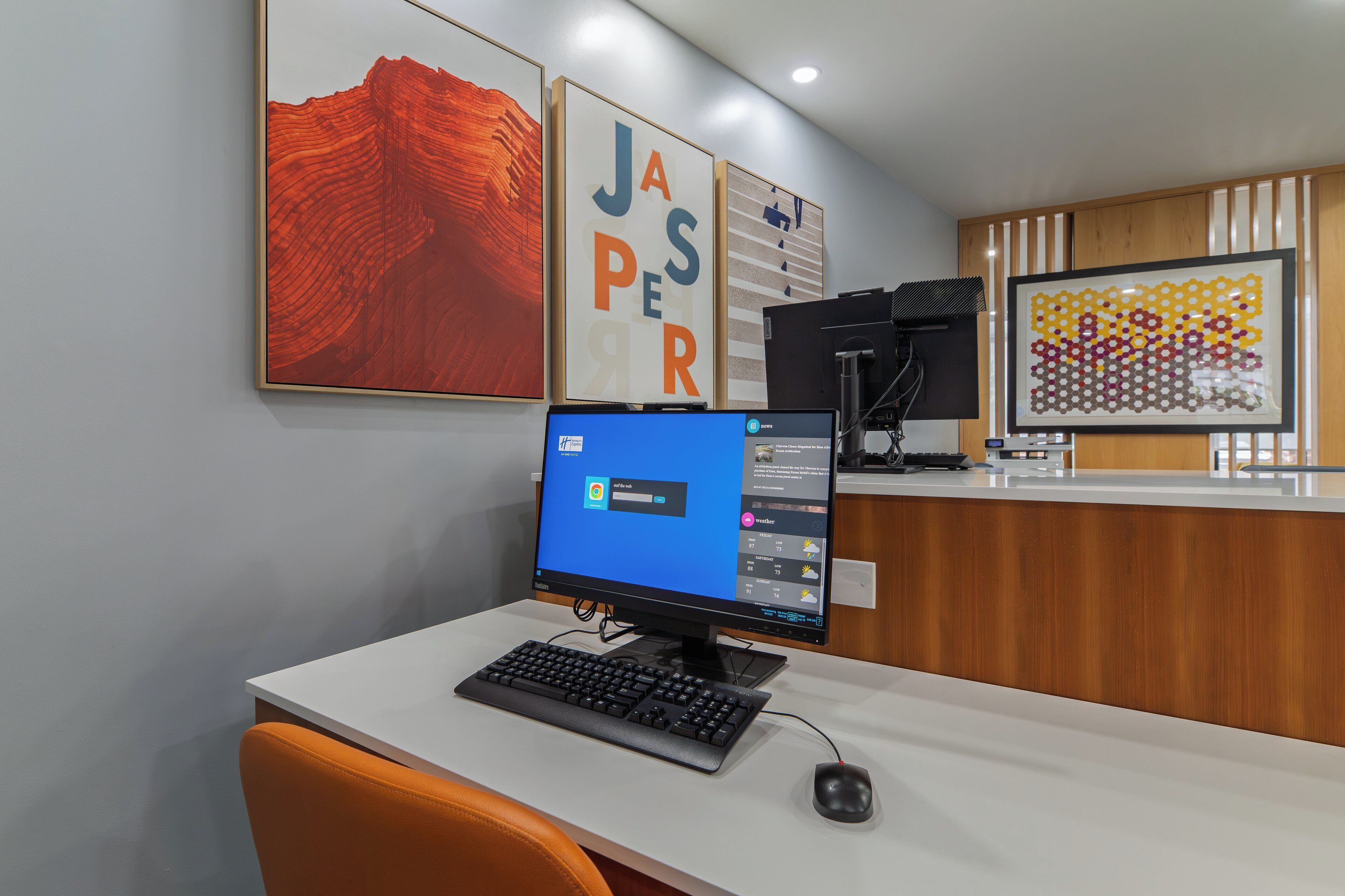 Ein Empfangsschalter mit Computer, Tastatur und Maus. Dahinter an der Wand befinden sich drei gerahmte Kunstwerke.