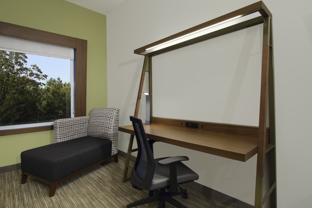 A room with a desk, a chair, a sofa, and a window with a view of trees.