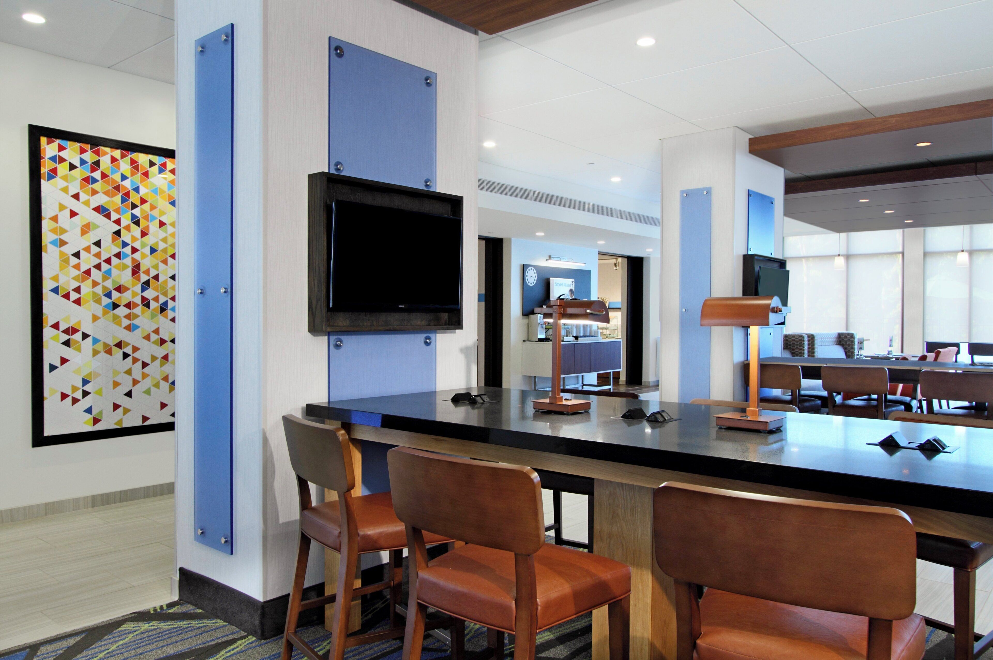 A modern hotel lobby with a reception desk, seating area, and a large flat-screen TV mounted on the wall.