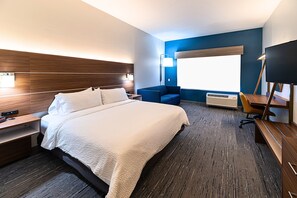 A hotel room with a large bed, a desk, a chair, a TV, and a window.