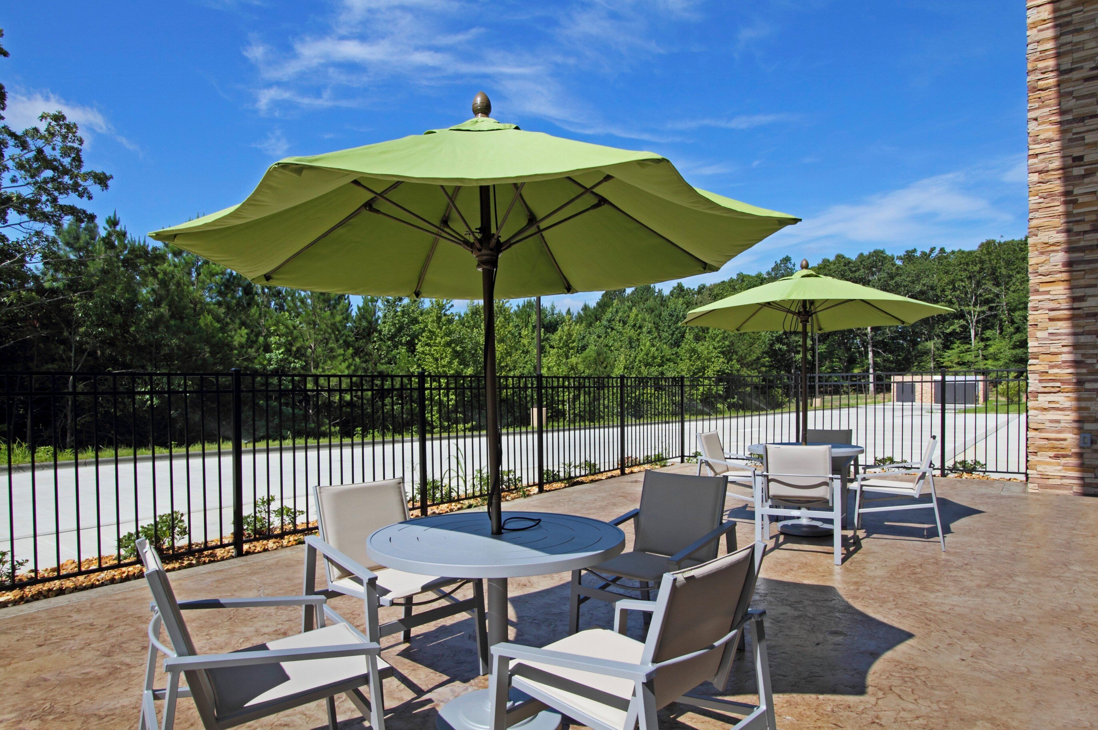 An outdoor patio with round tables and chairs, green umbrellas, and a stone wall.