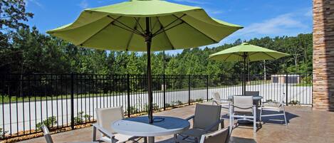 An outdoor patio with round tables and chairs, green umbrellas, and a stone wall.