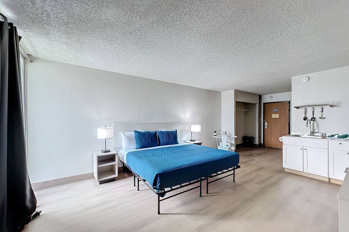 A hotel room with a bed, bedside tables, a desk, a chair, a wardrobe, and a bathroom.