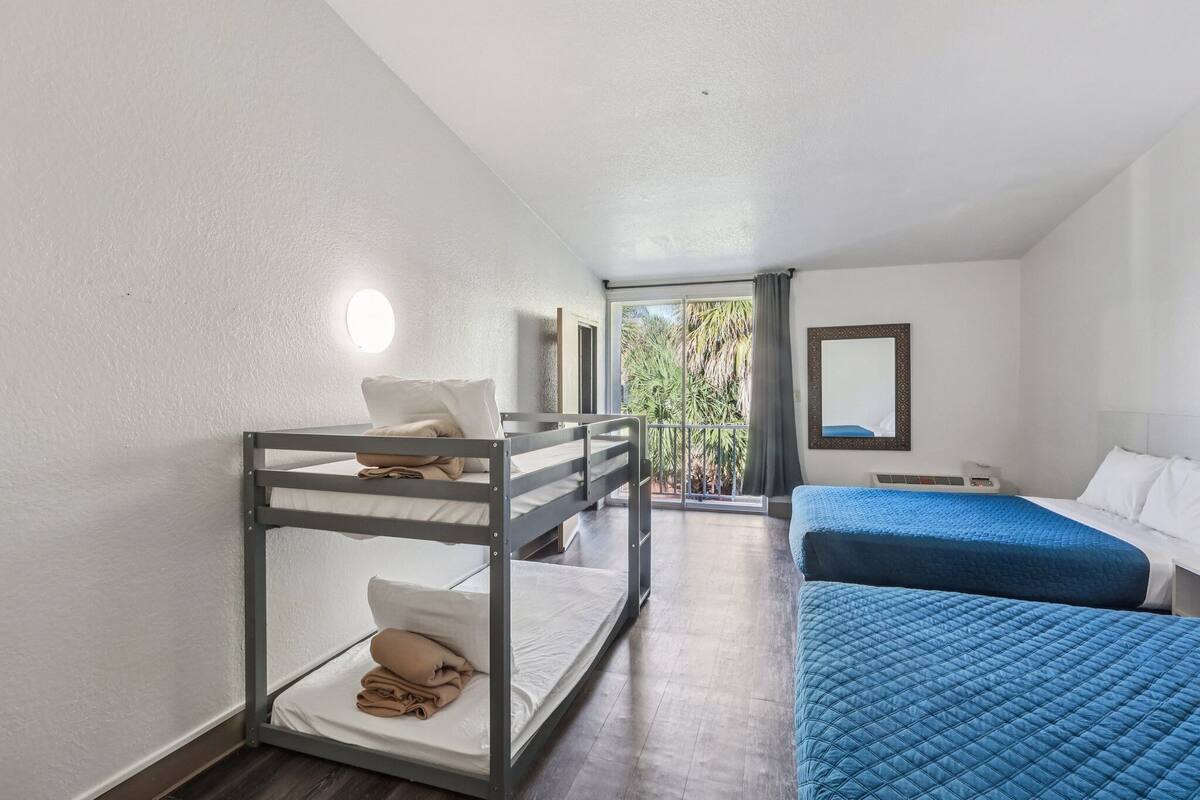 A room with bunk beds, a large window, and a view of greenery outside.