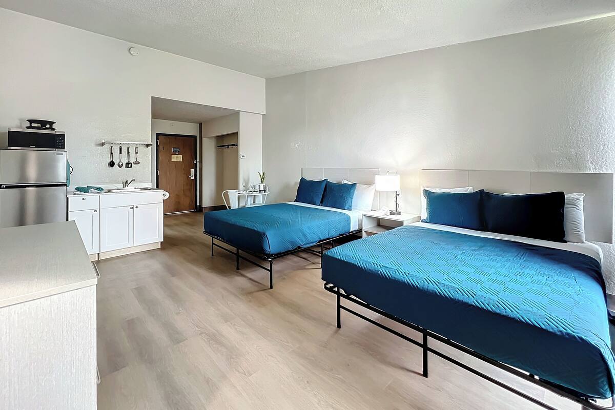 A hotel room with two beds, a kitchenette, and a bathroom.