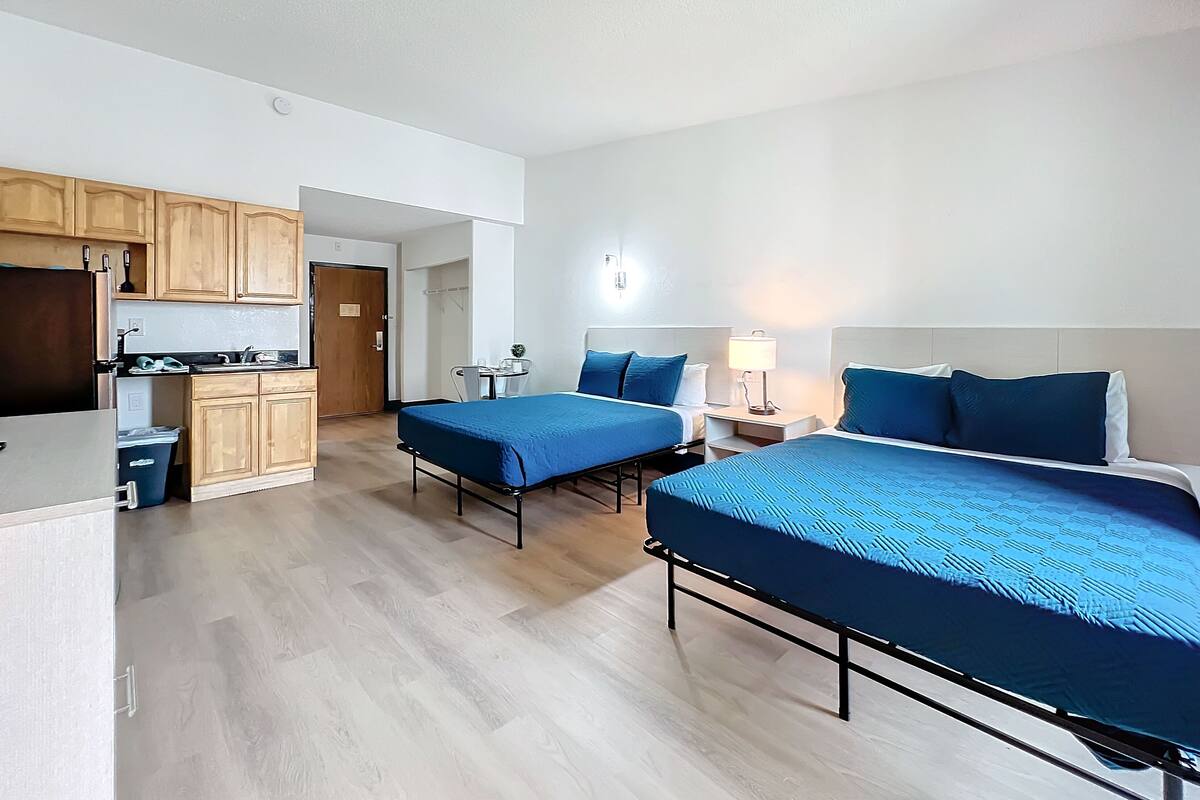A hotel room with two beds, a kitchenette, and a small dining area.