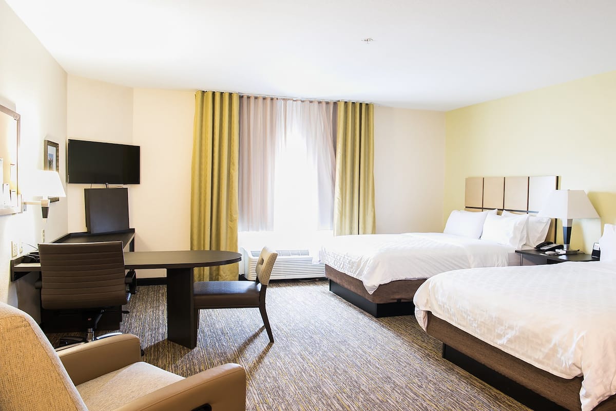 A hotel room with two beds, a desk, a chair, a TV, and a window with curtains.